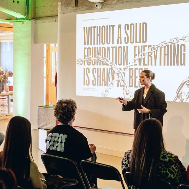 A speaker presenting on stage under the line 'Without a solid foundation, everything is shaky'