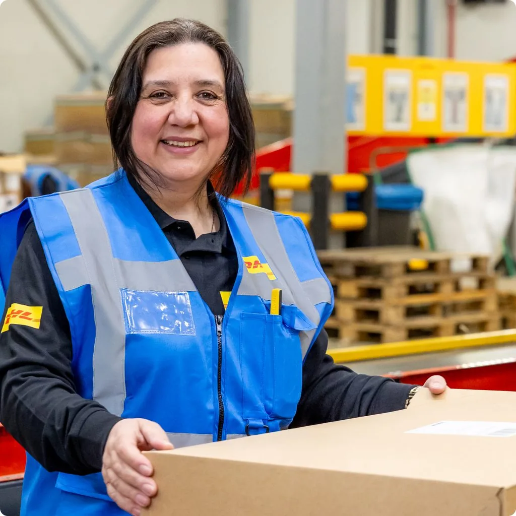 A DHL warehouse colleague in a hi-vis vest, carrying a parcel